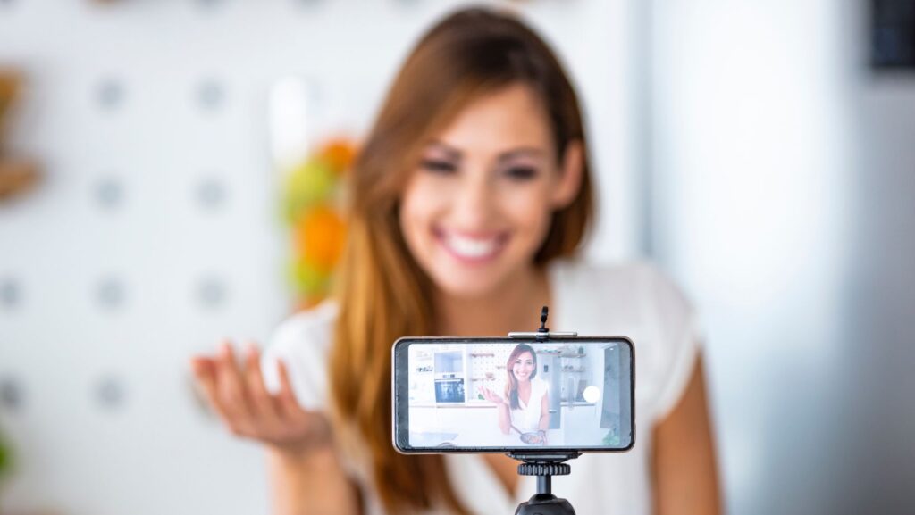 Menina  em frente à câmera de celular, gravando vídeo criando conteúdo mostrando autoridade para converter em compras